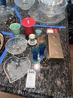 Overview of lot showing all items including clear glass candy dishes, colored glassware, candle holders, and metal match holder with matches