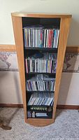 Front view of wooden CD cabinet filled with jewel case CDs on four shelves and bottom section