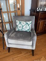 Front view of gray velvet accent chair with a rectangular decorative pillow with green and white circular pattern on seat.