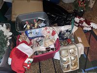Photo showing multiple plastic bins containing various Christmas table linens, stockings, ornaments, garlands, and artificial greenery items.