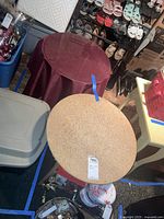 Photo showing two round craft tables positioned next to each other, one with cork surface and wooden legs, the other draped with a red fabric and glass top underneath.