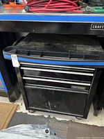 View of the Craftsman tool chest showing black metal with two drawers and compartment below, integrated under a workstation with blue accent trim.