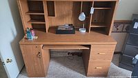 Front view of wood finish desk with hutch showing open workspace, lockable cabinet, drawers, and shelving filled with some items not included.