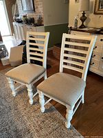 Two side chairs placed side by side showing ladder-back slats and upholstered seats.