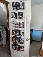 Over-the-door white metal DVD rack filled with multiple DVDs spread across four shelves. Visible titles include Ted, The Fighter among others.