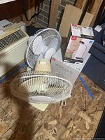 Various angles of two oscillating fans, Woozoo fan box, and desk lamp box on plywood floor.