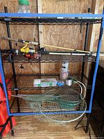 Metal shelf with four fishing rods with reels of various colors, fishing accessories such as fishing line, lure, and storage containers on middle and bottom shelves.