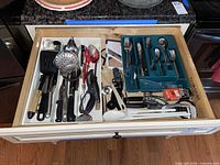 Top view of drawer with cooking utensils including spatulas, strainers, knives, scissors, mandolin, flatware in blue tray