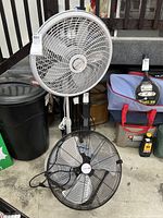 Lasko white pedestal fan and black Utilitech floor fan placed side by side on the floor.