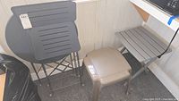 Two metal folding chairs stacked in front of folded round metal bistro table, plastic side table, and folding tray table