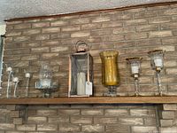 Full view of all nine candle holders and lantern displayed on a wooden shelf against a brick wall.