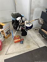 Golf bag standing on floor with multiple golf clubs inside and two boxes of golf balls placed in front.