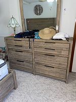 Front view of large wooden dresser with six drawers, topped with various clothes and a straw hat, and large matching mirror above it.