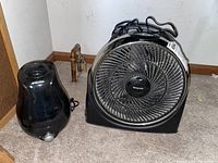 Honeywell fan and Microban humidifier positioned on carpeted floor near wall corner, showing side by side items with power cords visible.
