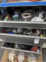 Metal drawers containing assorted hardware items including hose clamps, rolls of tape, quick connect nozzles, wires, and adhesives.