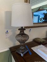 Front angle view of the decorative table lamp showing the cracked metallic urn-shaped base and white fabric drum shade.