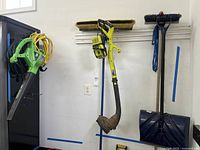 Photo of green Expert leaf blower, yellow Ryobi weed trimmer, broom and snow shovel hanging on wall