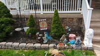 Photo shows front view of lawn decor arranged along garden bed edge with various figurines and blue fish sculpture.