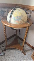 Standing globe on wooden tripod stand with twisted legs and triangular base.