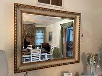 Front view of rectangular gold-tone framed mirror hanging on wall reflecting dining room furniture and decor.
