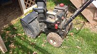 Photo showing MTD Snow King snow blower placed on grass near outdoor stairs, side view showing intake chute, engine and controls.