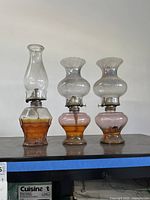 Three vintage hurricane oil lamps displayed side by side on a shelf.