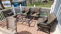 Four metal frame outdoor chairs with brown cushions placed on wooden deck around a metal frame table missing top pieces, lake view background.
