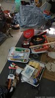 Lot of assorted painting supplies on table including orange bucket, folded tarp, roller pans, brushes in packaging