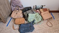 All purses and backpack grouped together on floor in front of wall to show entire lot