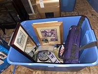 Blue bin containing framed photos, medallion collection, travel stadium seat cushion, garden flag, ornaments, and mirror.