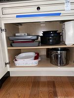 Open cabinet shelf showing stacked roasting pans and baking pans including CorningWare dish and black speckled roasters