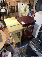 Two wooden side tables, one yellow and one brown, shown together with visible wear, placed on floor surrounded by other items.