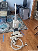 Full view of the vintage upright vacuum on a hardwood floor with attachments laid out in front.