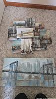Multiple multi-dimensional cityscape canvases in muted colors arranged on carpet, showcasing layered urban scenes with bridges and city buildings