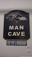 Photo showing the Baltimore Ravens Man Cave sign with the Pop Pop's Workshop sign below it on a wall.