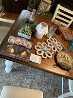 Photo showing wall art panels including 'LOVE' candle holder glass design, fruit art panels with apple and pear, two flower design panels, faux plants, white ceramic candle holder, glass vase, decorative flower items, and a sailing ship plate on a wooden table.
