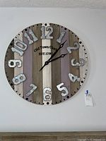 Front view of round wall clock with large metal numbers, rustic wood panel background and black hands. Clock marked "Old Town Clock EST. 1783"