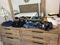 Nine women's swimsuits in size 15 and some sun hats displayed on wooden dresser in front of mirror