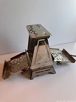 Antique metal toaster showing top and fold-out bread holders with decorative perforated metal sides