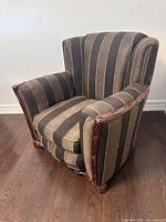 Front angled view of antique arm chair showing brown and beige vertical stripes and carved wooden frame with feet.