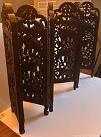 Image showing the side and angled view of the wood folding screen, displaying the carved legs and folded form of the panels.