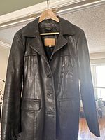 Front view of Danier black leather jacket displaying button closure, collar, and front flap pockets.