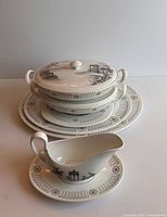 Photo of the set showing covered serving bowl, large plate, gravy boat and saucer with black and grey scenic design.