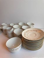 Fine bone china tea set arranged with cups, saucers, creamer, and sugar bowl. White with gold ornate pattern.