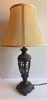 Photo showing antique style table lamp with beige fabric shade and ornate carved base