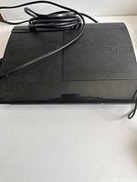 Black PlayStation 3 console with power cable laid on surface.
