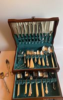 Open wooden case showing upper and lower compartments with silverware organized in velvet slots.