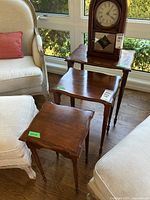 Front view of three nested tables alongside upholstered chairs, showing varying sizes and scalloped edges