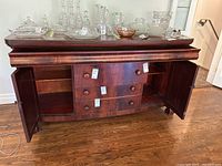Front view of antique sideboard with both side doors open revealing interior shelves and four central drawers.
