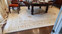 Full view of beige area rug under dining table showing floral patterns and geometric border.